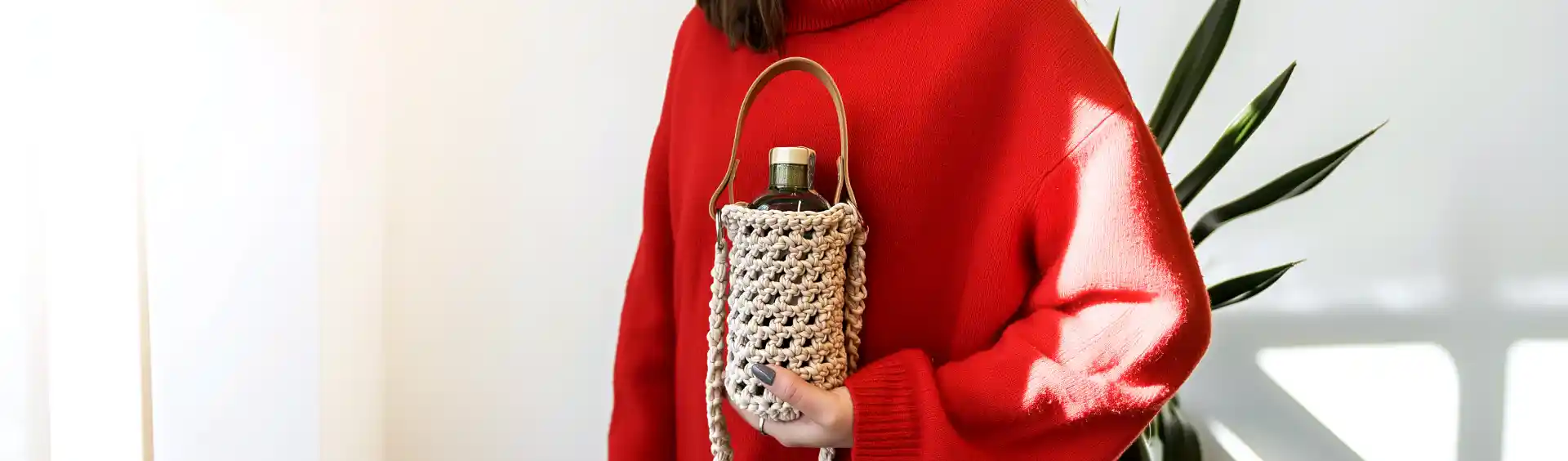 slečna v červeném svetru drží háčkovaný nosič na víno